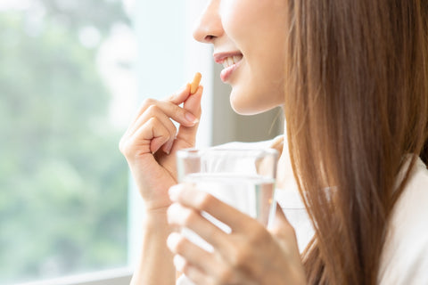 Frau nimmt Nahrungsergänzungsmittel mit einem Glas Wasser ein