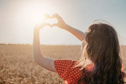 Frau macht mit Fingern ein Herz vor der Sonne