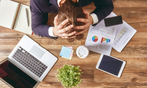 Ein Mann schlägt vor lauter Stress am Arbeitsplatz die Hände über dem Kopf zusammen