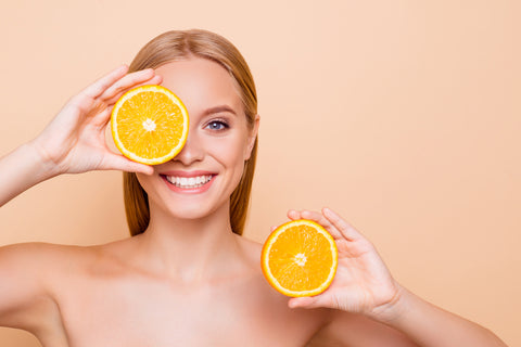 Frau hält sich zwei Orangenhälften vor den Körper