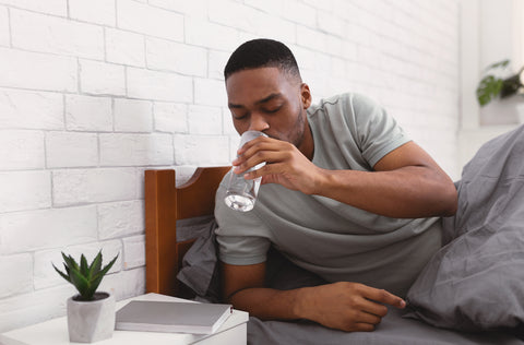 Mann trinkt ein Glas Wasser im Bett