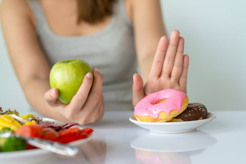 Frau isst einen Apfel und schiebt Teller mit Donuts weg