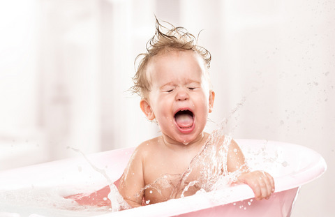 Baby bathing in bath tub with water splashing and bubbles in his hair.