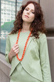 Our model, Jessie, is wearing our Overlapping Front Jacket in Sage Green with matching Drop Sleeve Scallop Hem Dress accenting the look with long chain necklace in orange.