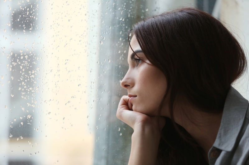 Sad woman looking outside window in the rain