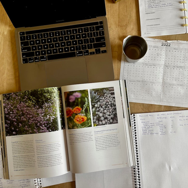 Picture of computer, lists and books, showing the process of garden planning for planning for growing perennial flowers and herbs from seed