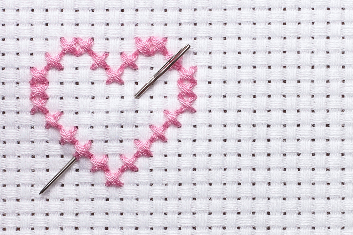 pink embroidery thread in cross stitch heart with tapestry needle on white fabric
