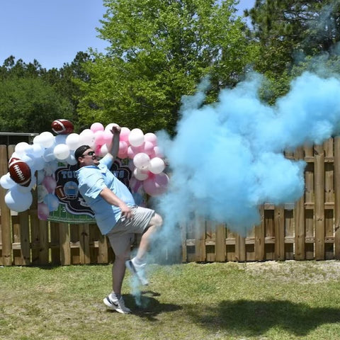 Dad gender reveal moment with a football at the gender reveal party kicking it and blue powder flying out