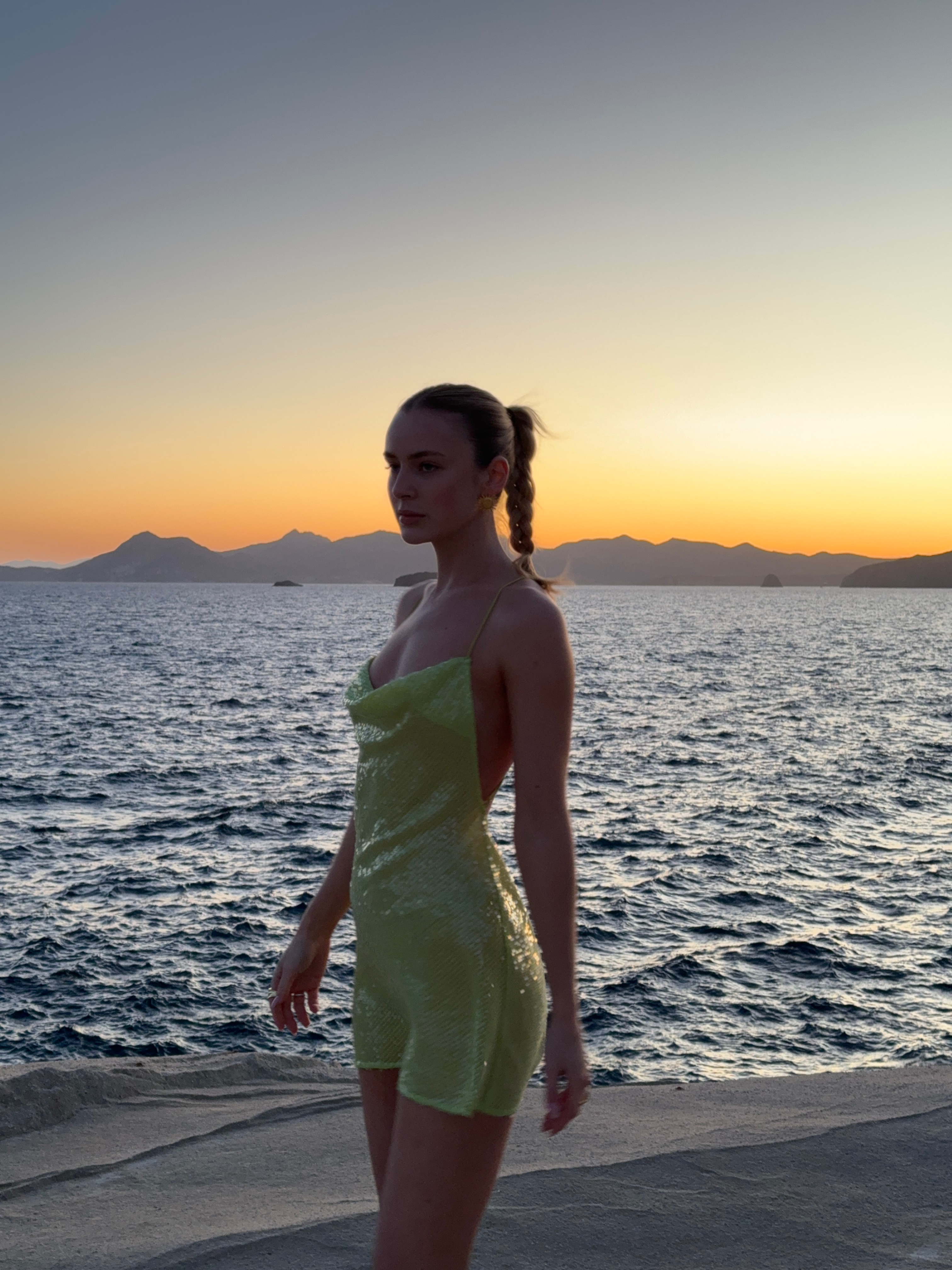 Our social media manager stands gracefully near the beach in a stunning green shimmery resort wear dress, exuding seaside elegance with a different pose.