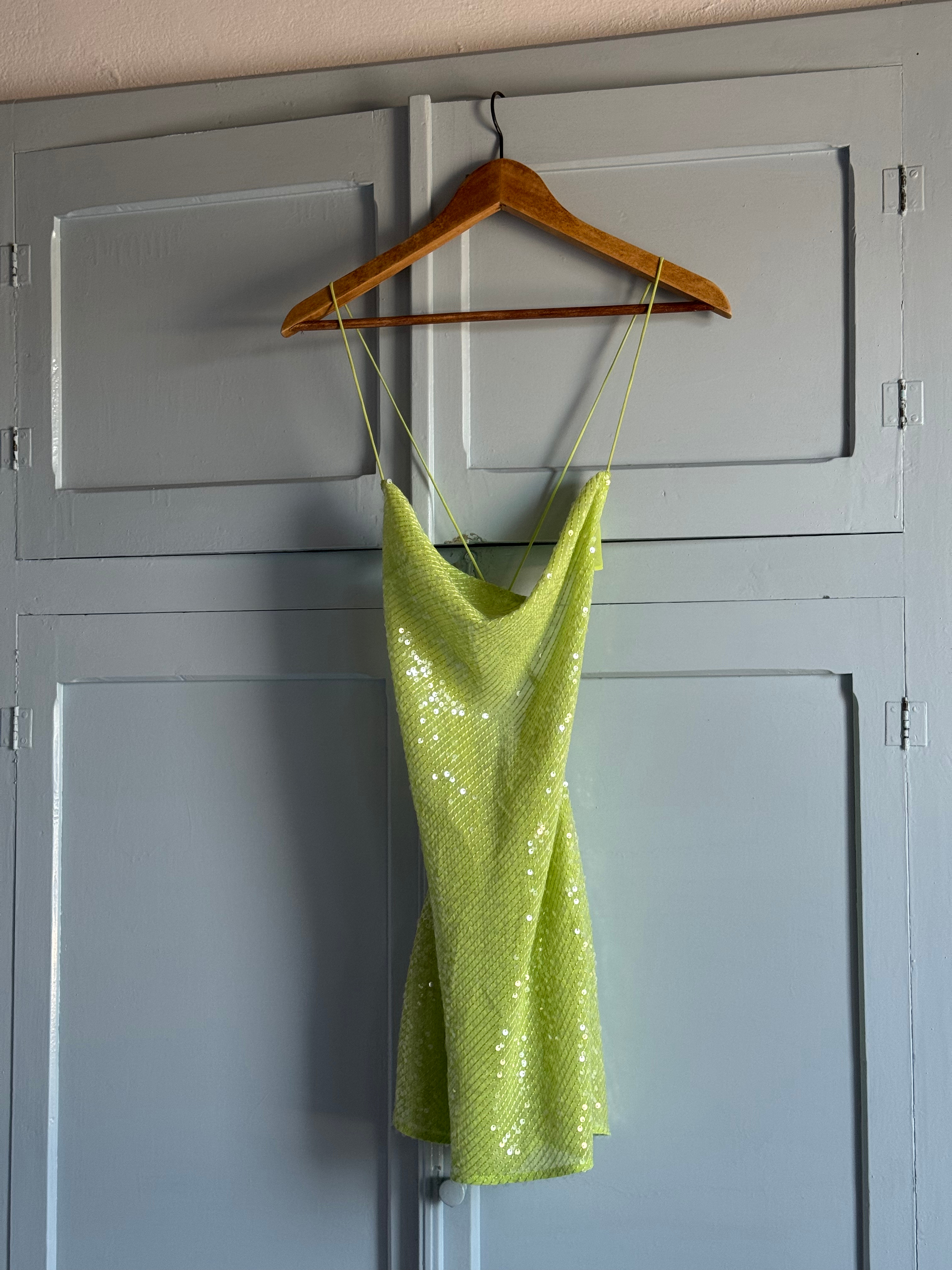 Enhancing the hotel room's decor, a green shimmery dress hangs gracefully, adding a touch of sophistication to the interior