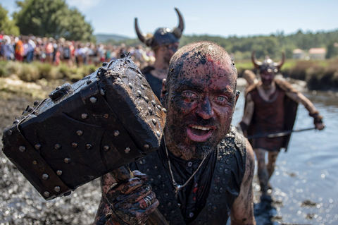 A man in Viking apparel stands in a river taking part in a battle reenactment. He has mud on his face and holds a Mjolnir, known as Thor's hammer. He wears a Viking inspired necklace around his neck, an example of ancient Norse jewelry