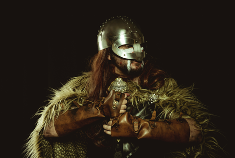 A modern-day Viking wearing a helmet and fur cape, emboldened by symbols like those on a Helm of Awe necklace.