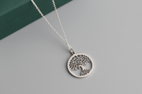 A stainless steel tree of life pendant on a silver chain sits against a plain grey background