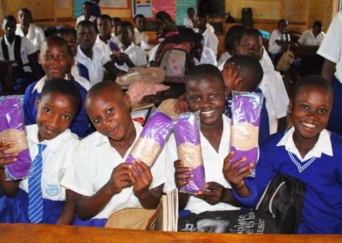 Girls' in Uganda holding their new, purple, reusable period products and menstrual pads donated by Just a Drop