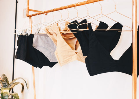 Black, grey and almond organic cotton bralettes and underwear hang on copper hangers from a copper rail