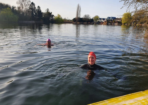 Sarah is in the bottom right corner, swimming outdoors in a deep blue lake. She's wearing a pink swimming cap and there is another swimmer to the back and right of her