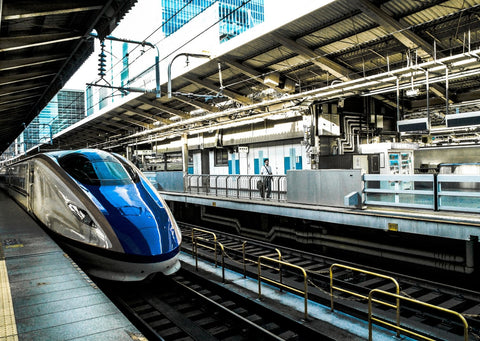 In a train station, a curved blue modern train waits at the platform