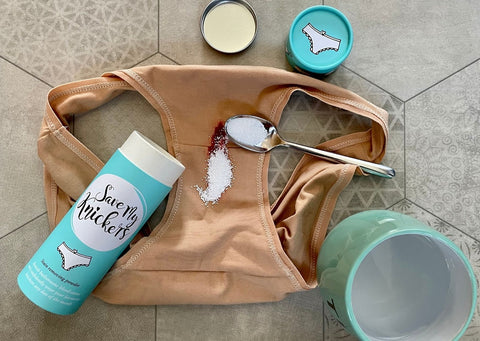 Organic Cotton Y.O.U underwear are surrounded by the Save My Knickers blue tube, a blue mug filled with water and a spoon is on the underwear