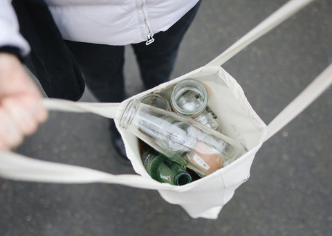 A reusable white bag contains glass bottles and eco-friendly swaps