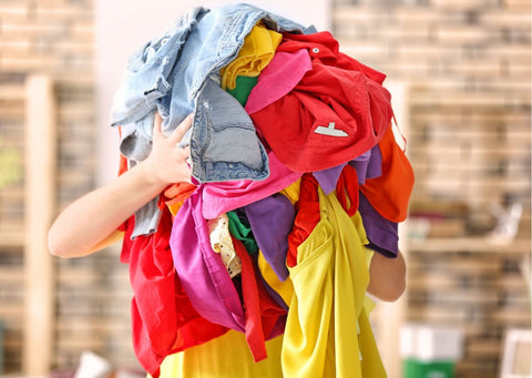 A person holds a bunch of brightly coloured clothes in front of their face