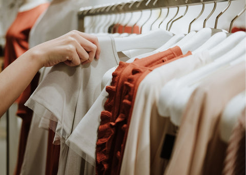 A hand picks out a shirt from a rail of beige, muted toned clothing