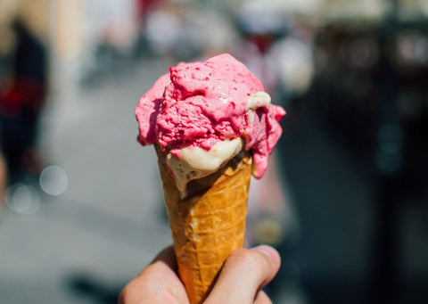 Someone holds an ice cream in a cone with a scoop of strawberry dolloped on top