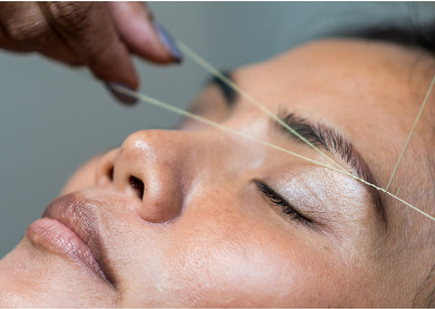 a woman's face, her dark brown eyebrows are being threaded