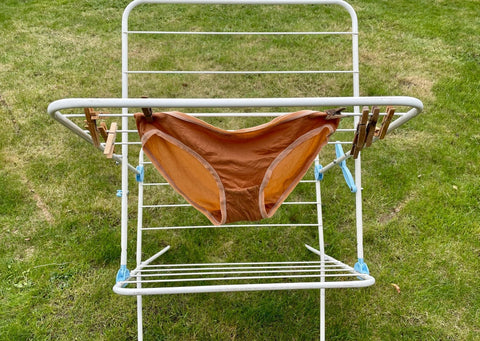 A pair of almond y.o.u underwear bikini bottoms hang in the garden on a clothes horse to dry