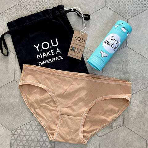 A pair of almond bikini bottoms with a teal bottle of save my knickers