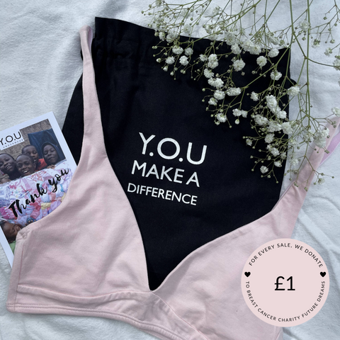 Our Light Pink Organic Cotton Bralette is on top of our 'Y.O.U Make A Difference' organic cotton black bag, there are white budded flowers in the top right corner 