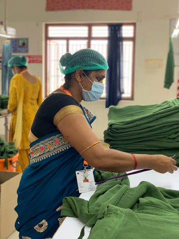 A lady sorts through a pile of green clothing in the factory