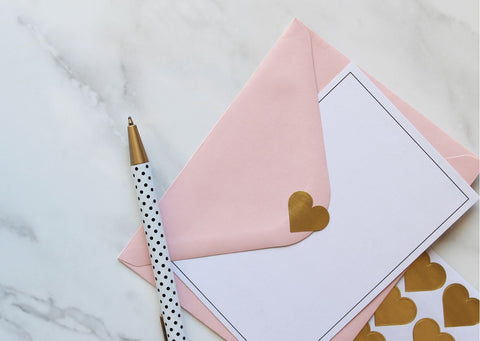 A pink envelope and blank note with a silver pen