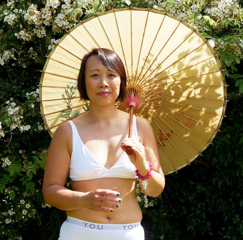 Lady wearing a white bralette and Y.O.U boy shorts, holding a bamboo parasol.