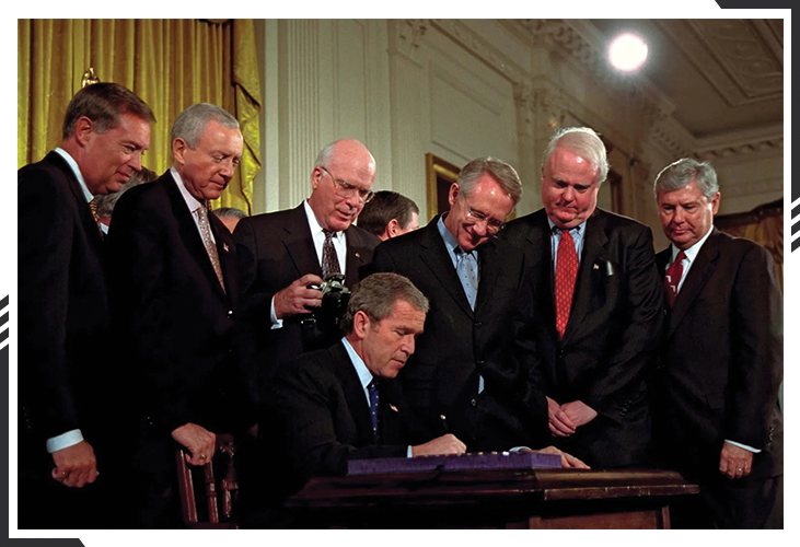 George W. Bush gleefully signing the PATRIOT Act into law, surrounded by supporters