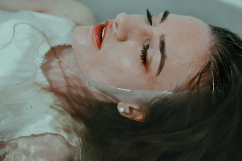 A woman lying on her back in water with her eyes closed