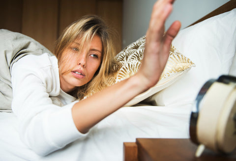 Woman about to hit the snooze button on her alarm clock