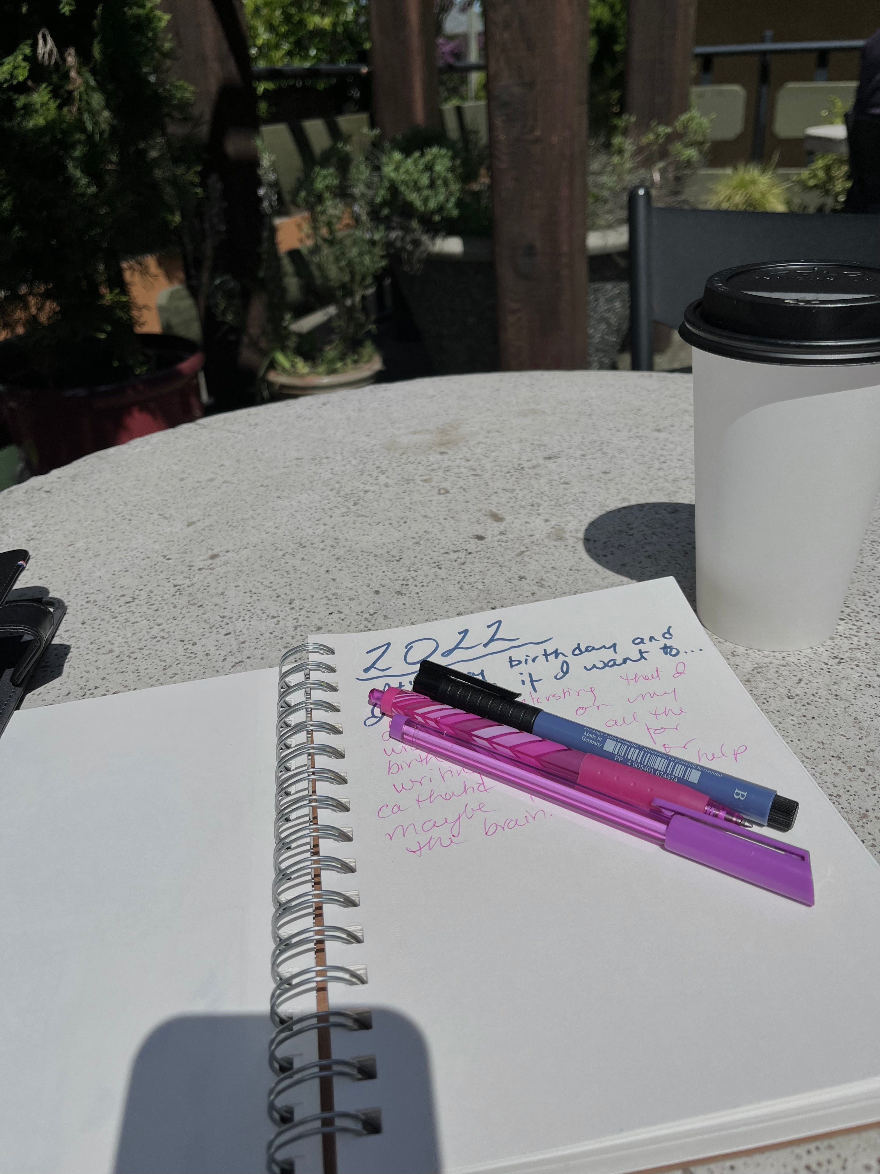 Journal on table with pink and purple pens and coffee