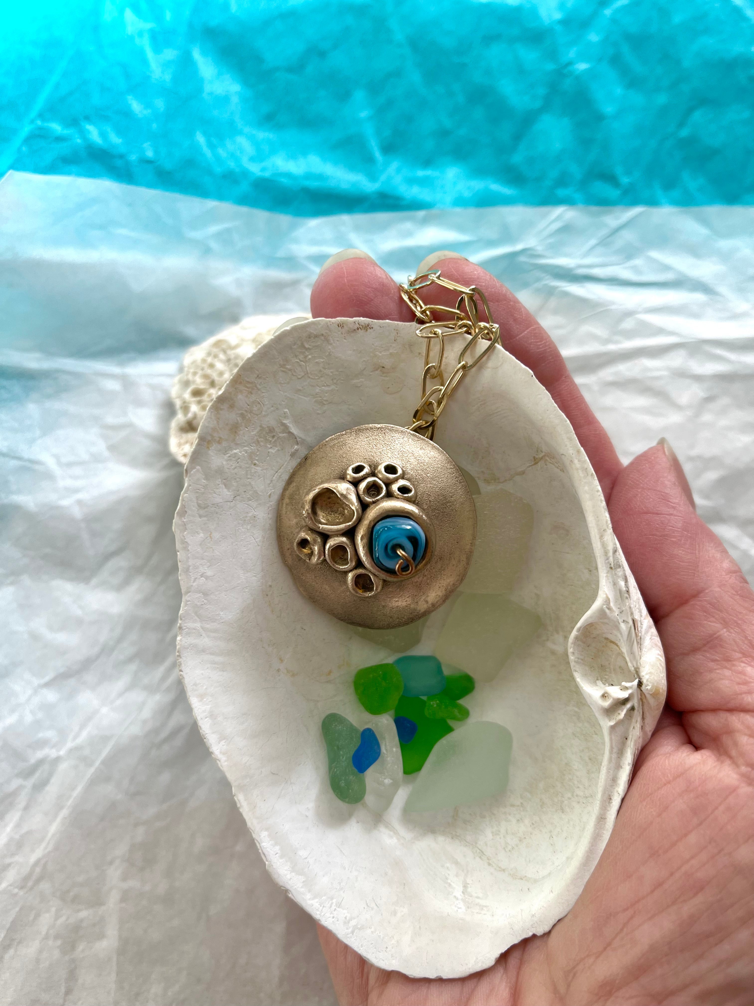 Handheld seashell with bronze necklace and coloured seaglass inside