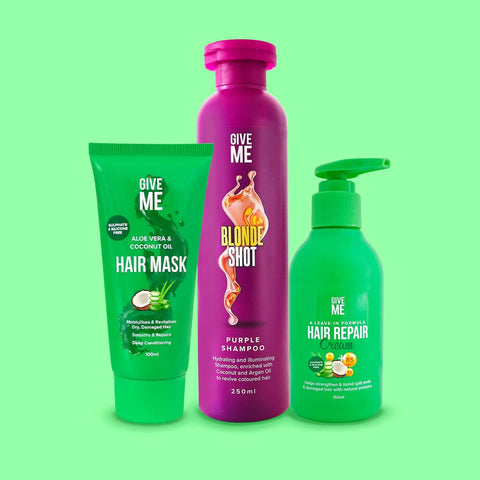 A dark purple bottle of the Give Me Cosmetics Blonde Shot -  Blonde Enhancing Toning Shampoo in between a green bottle of the Aloe Vera and Coconut Oil Hair Mask and a green bottle of the Aloe Vera and Coconut Oil Hair Repair Cream.