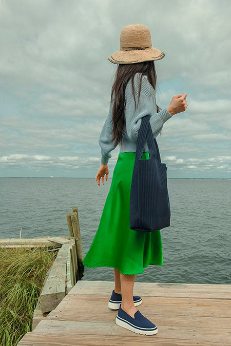 Woman wearing our Navy Knit Sneaker and Navy Sutton Tote Bag on a pier by the ocean