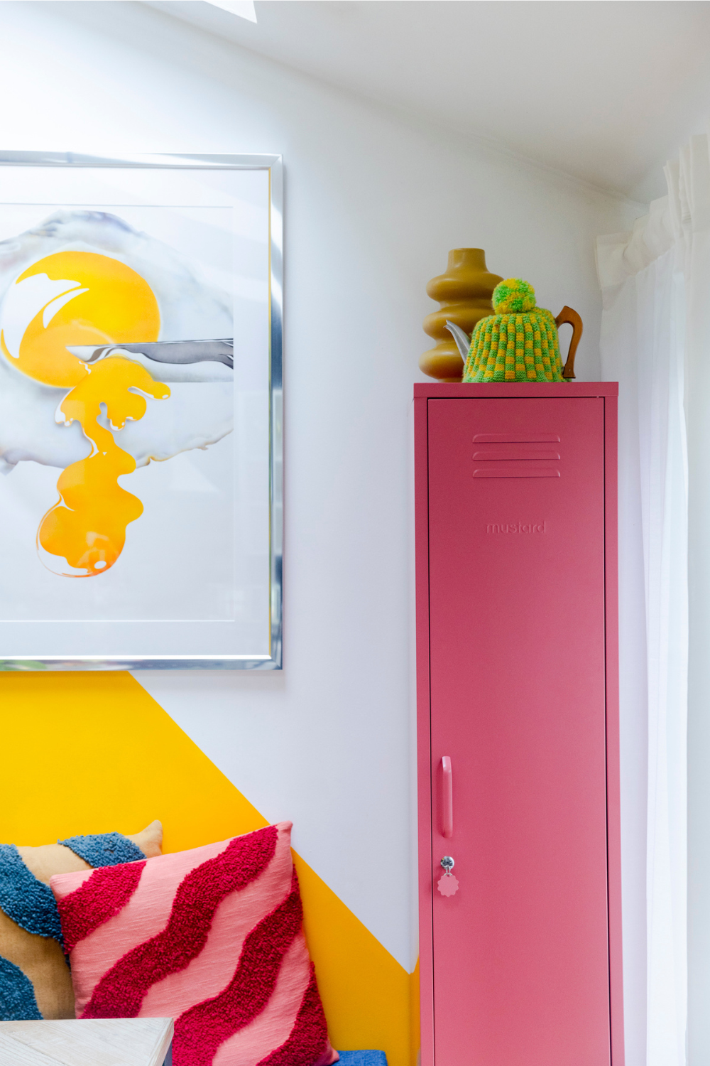 A Skinny in Berry is propped against a bright yellow wall with colourful wavy-patterned cushions on a bench next to them.