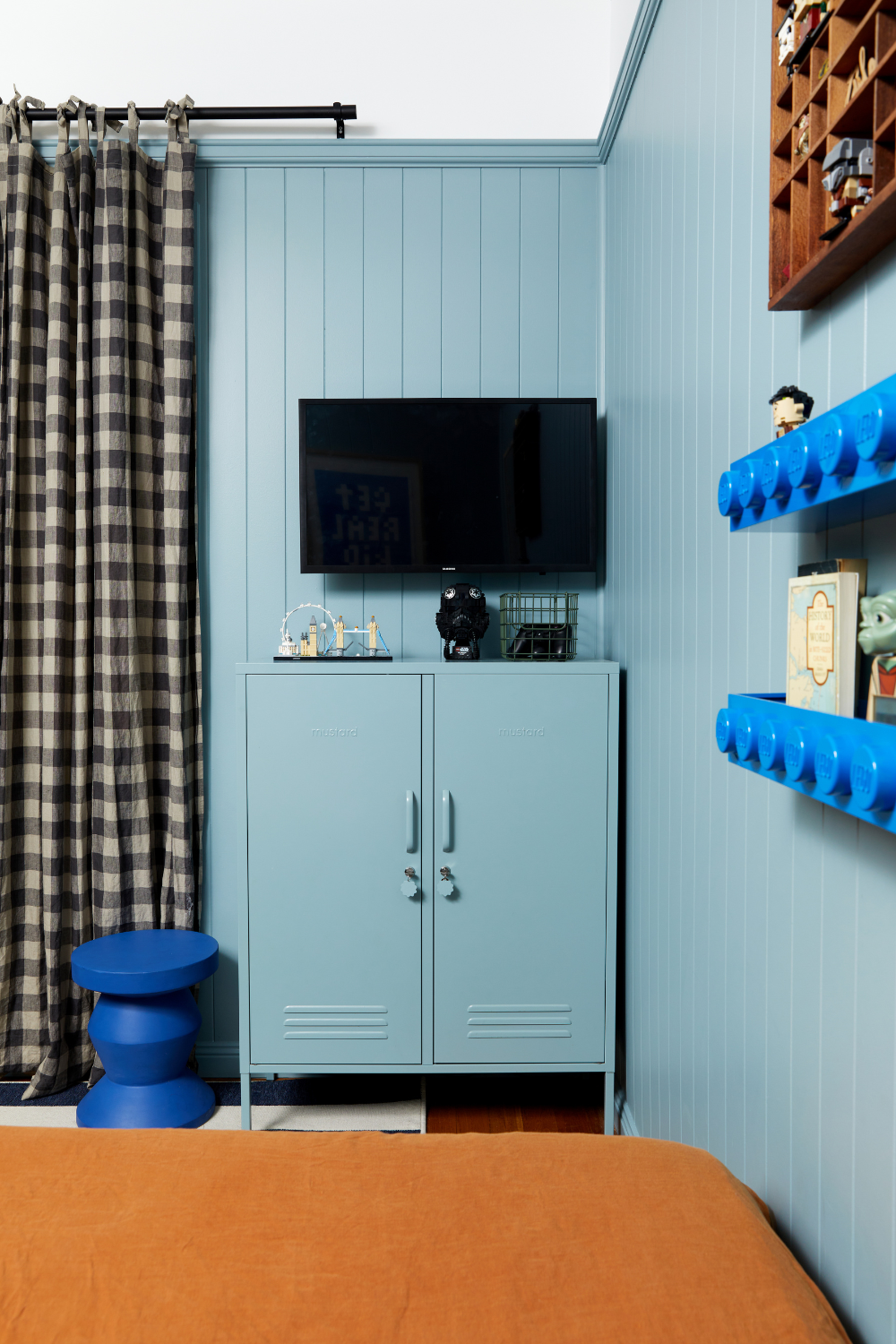 A small TV is mounted on top of an Ocean Midi and there are brown and white gingham curtains visible next to the locker.