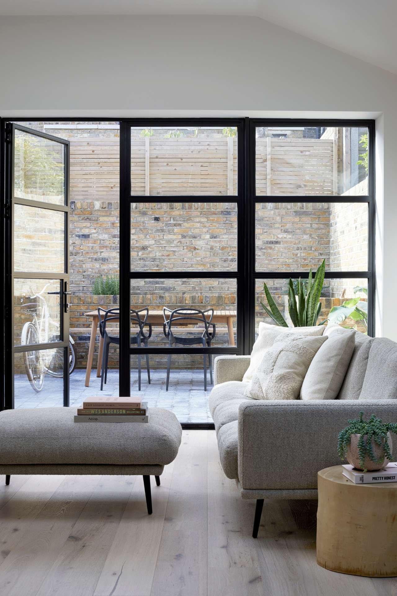 A large wall of windows looks out onto a paved courtyard with sculptural outdoor chairs arranged around a table.