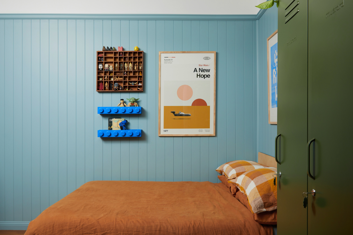 Dylan's bed sits against an Ocean blue wall. There is a lego shelf mounted on the wall next to a graphic poster.