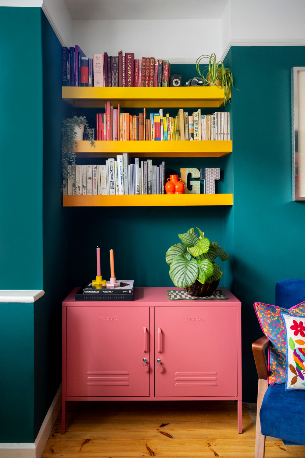 A Berry Lowdown is tucked into a nook in a dark teal room, below built-in yellow bookshelves.