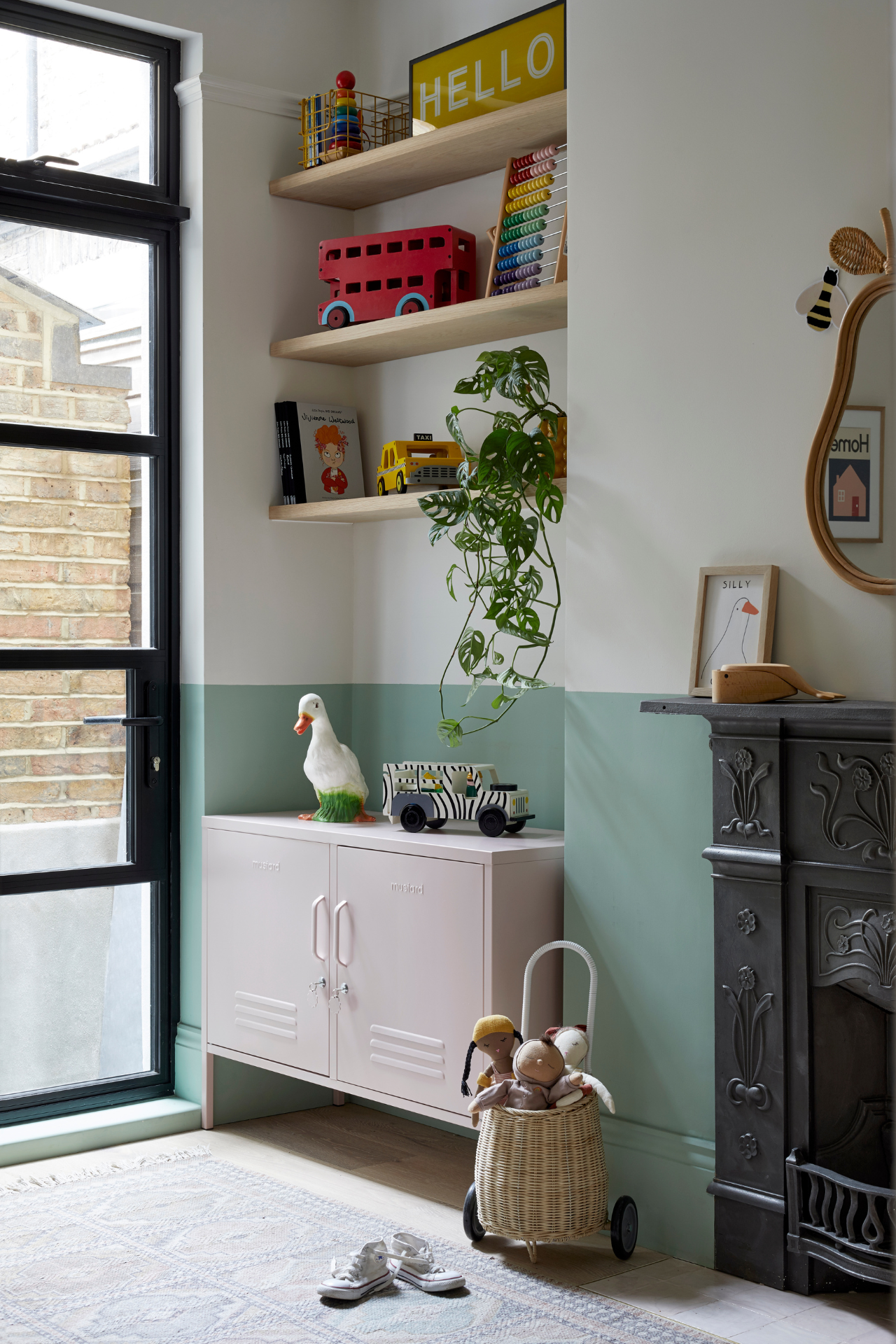 A nursery is filled with colourful wooden toys and splashes of colour arranged around a Blush Lowdown and a Black, ornate fireplace.