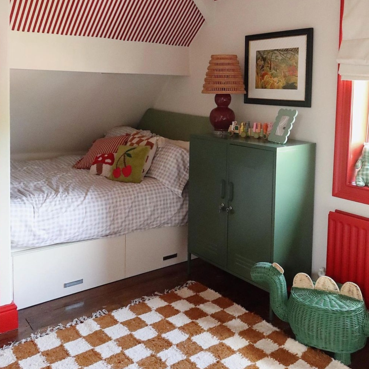 A bed is built-in to the corner of a small room with white walls and red skirting boards. There is an Olive Midi next to the bed and a brown and white checkered rug on the floor, with pops of red throughout the room.