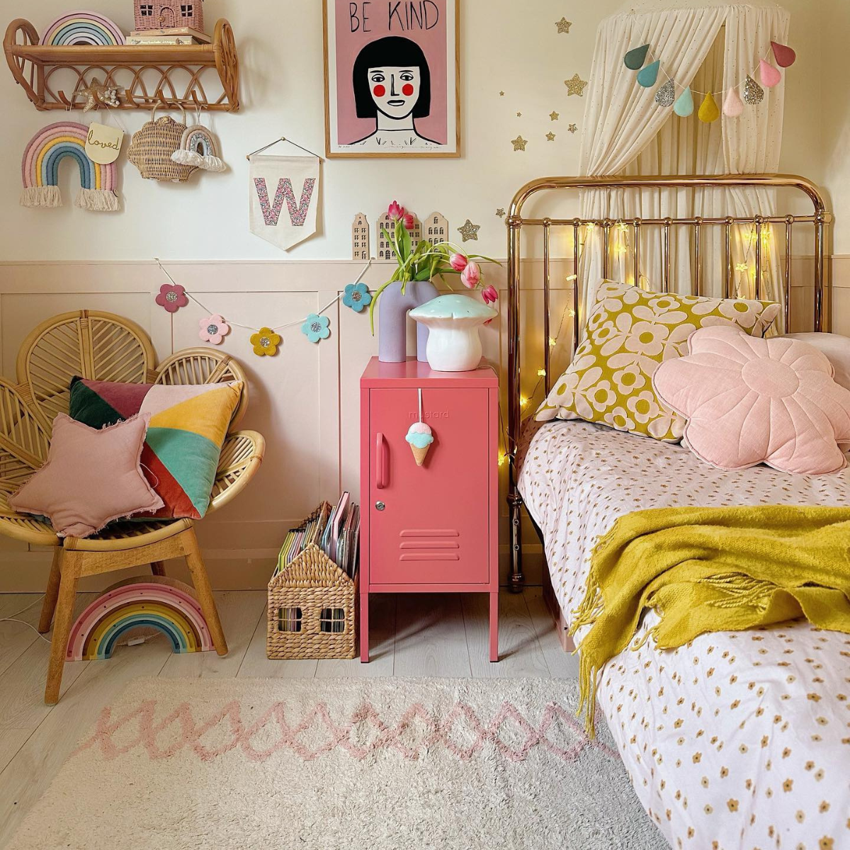 A rose gold single bed with a blush canopy sits in a soft pink and cream room. There are fairy lights wrapped around the bedhead and a Berry Shorty is arranged next to a cane chair in the shape of a flower.