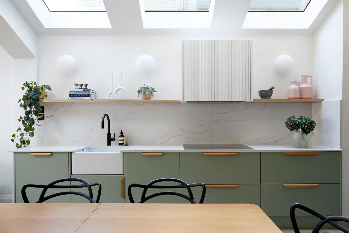 A wide shot of the sage green kitchen shows trailing plants and blush pink accents on the custom wall shelving.