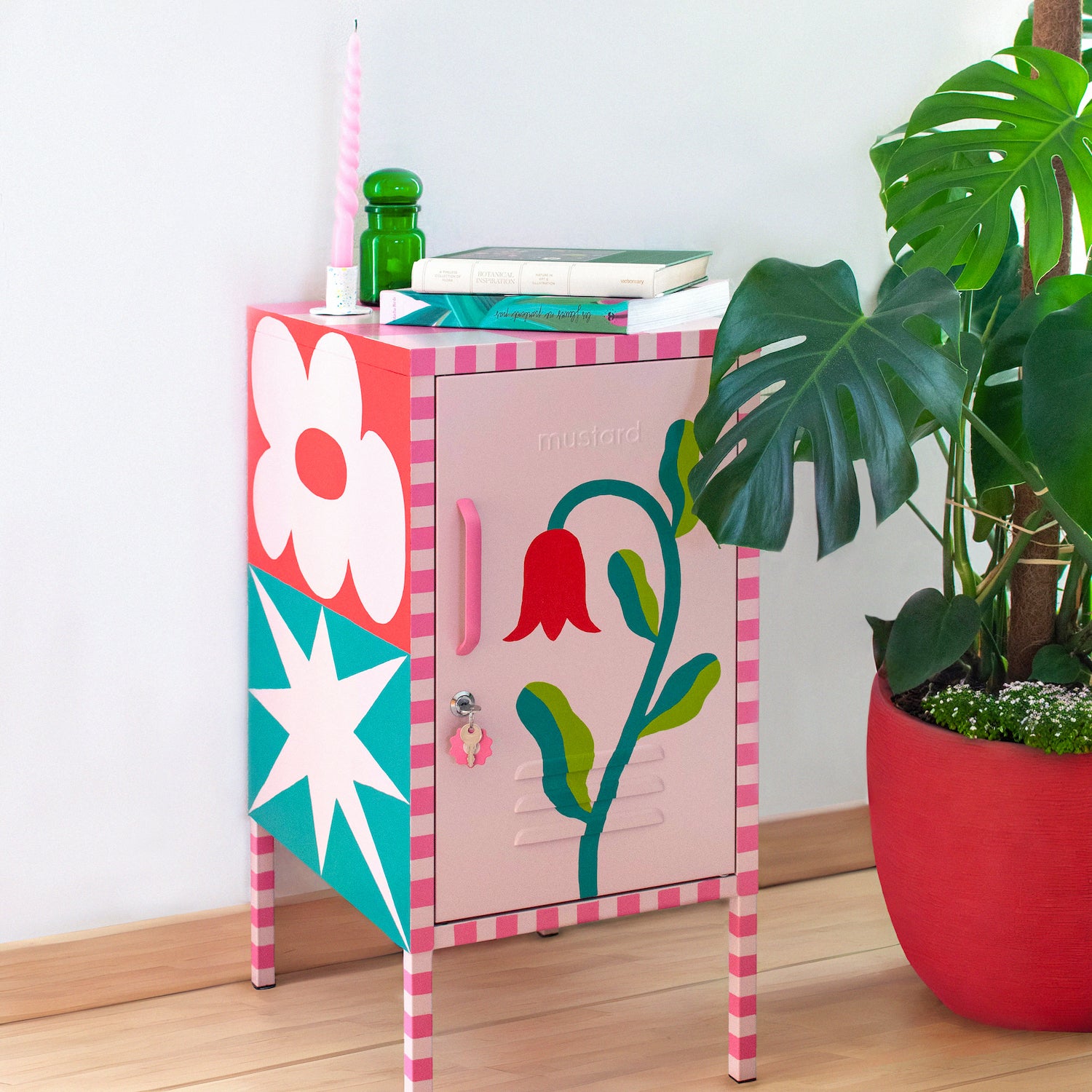 The finished Shorty sits against a white wall with a monstera plant in a red pot next to it. There is a large flower painted on the front, with checkerboard details on the edges and a star on the side.